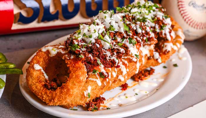 A bar favorite: a giant fried onion ring topped with chili, cheese, and sour cream on a white plate.