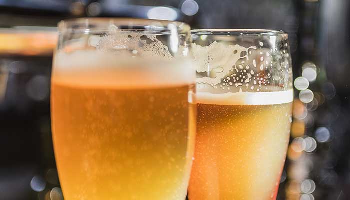 Two glasses of frothy, light amber beer with bubbles at a restaurant, perfect with pizza.