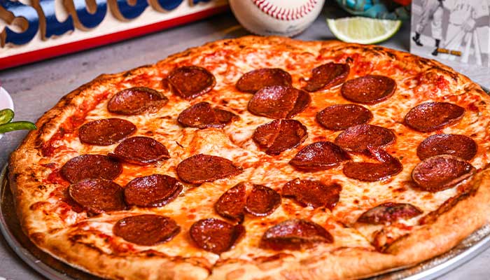 Pepperoni pizza on a tray at a Tucson restaurant, with chicken wings and baseball in the background.