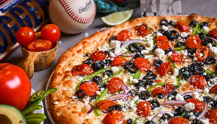 A veggie pizza with olives, tomatoes, and cheese at a Tucson restaurant, with baseball décor.