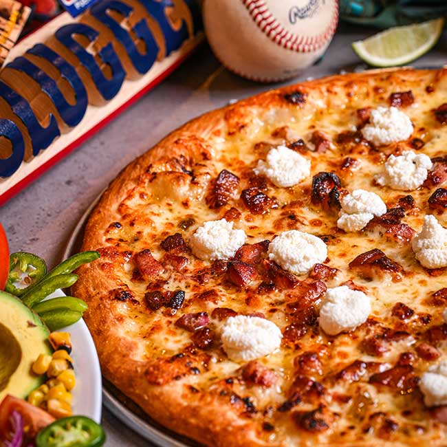 Close-up of a pizza with ricotta and bacon at a restaurant, baseball bat and ball in background.