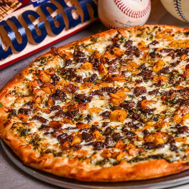 A restaurant-style pizza with chicken, cheese, herbs, onions, and a bar-themed backdrop.