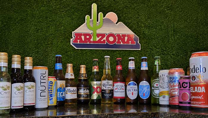 Assorted beer bottles and cans lined up at a Tucson bar, with an Arizona sign and cactus design.