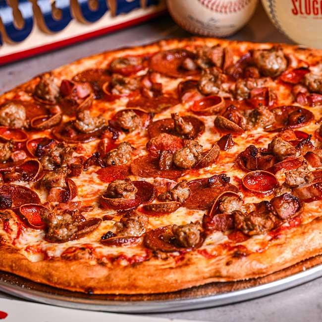 A pizza with pepperoni and sausage sits on a tray at a Tucson bar, baseballs in the background.