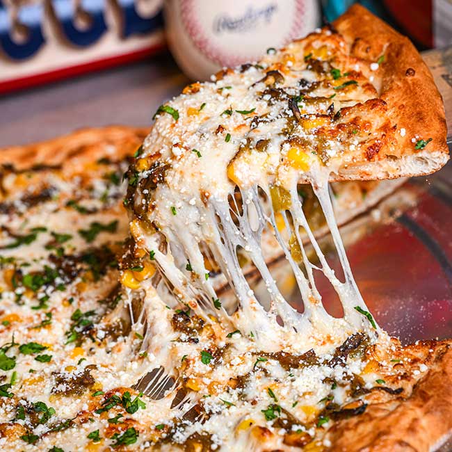 A cheesy pizza slice from a Tucson restaurant being lifted, with melted cheese stretching.