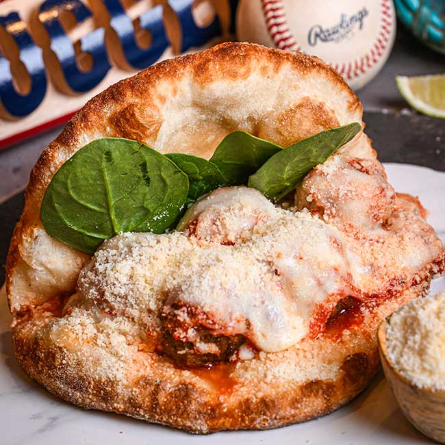 Meatball sub with melted cheese and spinach at a restaurant, baseball and bat in background.