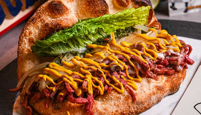Flatbread taco filled with shredded meat, lettuce, onions, and a hint of restaurant-style mustard.