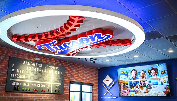 Baseball-themed bar and pizza spot with a Tucson sign, scoreboard, and TV on a brick wall.