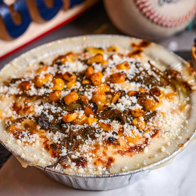 Cheesy baked casserole topped with corn, green peppers—Tucson restaurant classic in a foil dish.