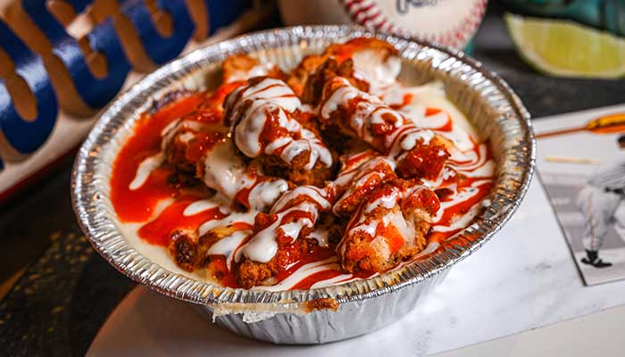 Fried chicken bites in a foil dish with creamy cheese sauce, perfect with pizza or chicken wings.